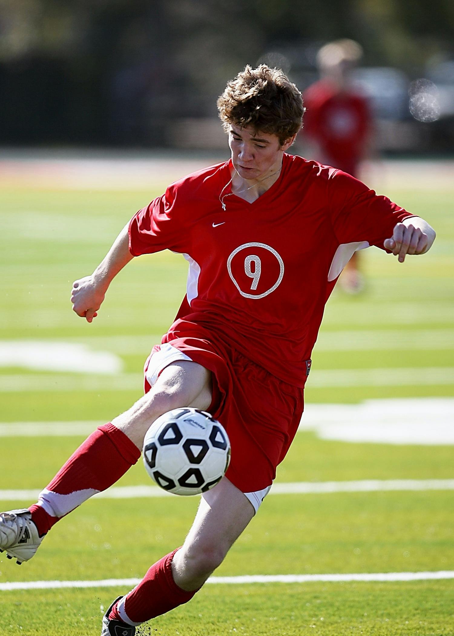Soccer player in red uniform kicking ball during a match outdoors.